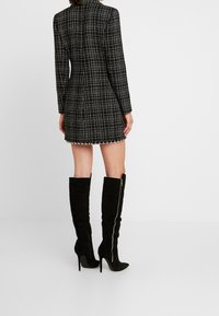 Black and white plaid dress with long sleeves and a fitted silhouette, paired with knee-high black suede stiletto boots.