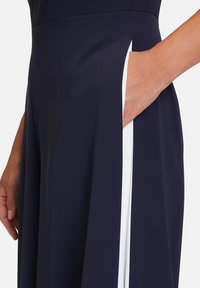 Robe marine avec un détail accent en blanc le long de la couture latérale, dotée d'une poche fonctionnelle visible près de la taille. Texture lisse.