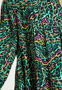 Vícebarevné šaty s živým zvířecím potiskem v zelených, černých, růžových a fialových tónech a s volnou, strukturovanou tkaninou.