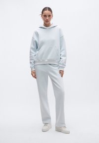 Conjunto de sweatpants e hoodie azul claro, com bolso frontal, punhos e bainha canelados, com um corte descontraído e textura de tecido macio.