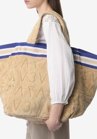 Beige badstof stoffen totebag met geperste letters, blauwe en crèmekleurige gestreepte accenten, grote maat, dikke schouderbanden en een gestructureerd oppervlak.