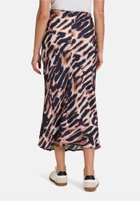 Jupe midi en imprimé léopard en tissu doux, présentant une silhouette fluide et une fente au dos. Assortie à des baskets blanches et des accents noirs.