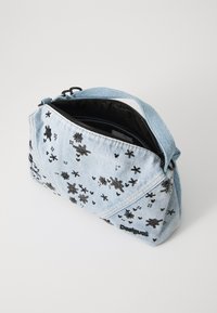 Borsa in denim blu con decorazioni floreali nere, chiusura a zip e una sola tracolla. Interno foderato in tessuto nero. Forma compatta e angolare.
