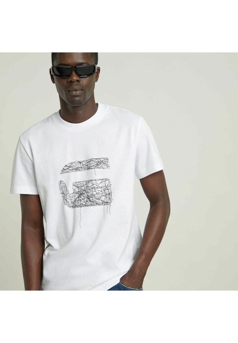 Camiseta de algodón blanca con un gráfico de líneas abstractas negras en el frente. Diseño de cuello redondo con mangas cortas.