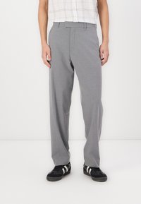 Un pantalon gris à coupe décontractée, avec une texture de tissu visible, doté d'un devant plat et de poches latérales, associé à des baskets noires.