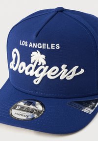 Capa snapback azul com "Los Angeles" e "Dodgers" bordados em branco. Apresenta uma viseira curvada e um autocolante do logotipo New Era na aba.