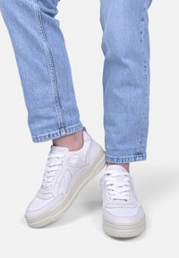 Hvide sneakers med en glat overflade, snørebånd fortil, tyk cremegulv og teksturerede detaljer, parret med lyseblå jeans.