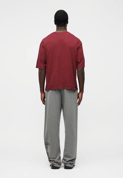 T-shirt vermelha de algodão com mangas curtas e corte descontraído, combinada com calças de fato de treino cinzentas largas com um gráfico impresso perto da bainha.