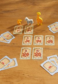 Wooden animal figurines (giraffe, zebra, parrot) on a wooden surface, surrounded by playing cards depicting barrels and apples in various quantities.