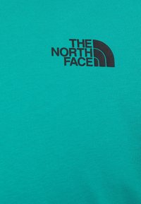 Turkusowa bawełniana koszulka z czarnym logo The North Face. Materiał ma gładką teksturę i prosty okrągły dekolt.