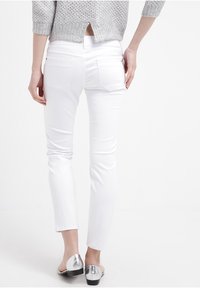 Jeans blancos ajustados con una textura de algodón suave, que presentan bolsillos traseros y una cintura de altura media, combinados con bailarinas plateadas brillantes.