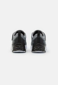 Des chaussures de sport noires et grises avec un dessus en maille texturée, un col rembourré et une semelle blanche avec un motif en zigzag sur le dessous.