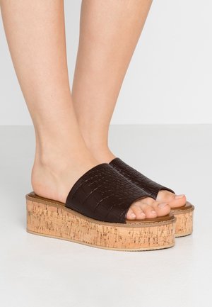 Kork platform slide sandaler med en mørkebrun tekstureret kunstlæderoverdel. Åben tå-design med subtile sømdetaljer.