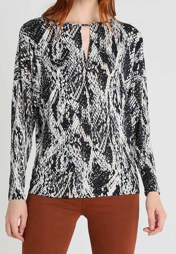 Koszula w czarno-białe wzory węża z dekoltem w kształcie dziurki, długimi rękawami i luźnym krojem. Miękki materiał z delikatnym połyskiem. Połączona z brązowymi spodniami.
