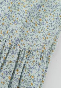 Jasnoniebieska tkanina z drobnym nadrukiem kwiatowym w kolorach pomarańczowym, fioletowym i różowym, z marszczonymi zakładkami wzdłuż szwu.