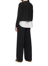 Veste noire cropped avec une finition texturée, portée sur une chemise blanche et associée à un pantalon noir ample. Présente un détail de dos plissé.