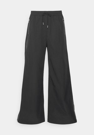 Zwarte wijde broek met een elastische tailleband en een trekkoord. Heeft zijzakken met rits en witte accentlijnen langs de zijkanten.
