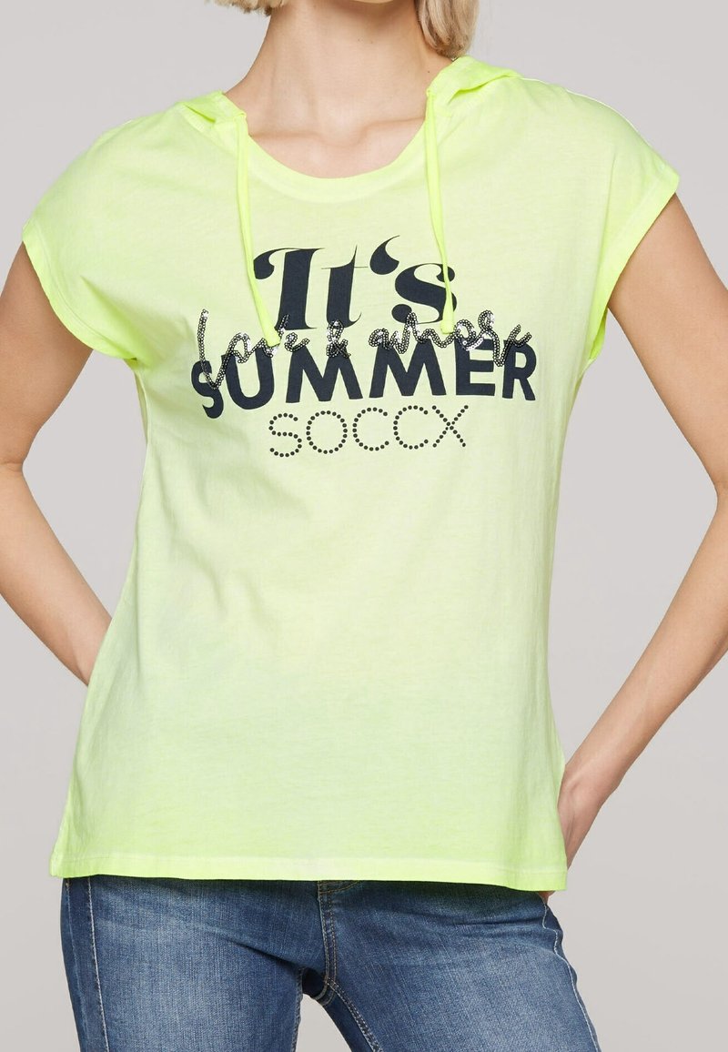 Chemise à manches courtes jaune fluo avec capuche, ornée d'un texte en noir "C'est l'été SOCCX" et de strass décoratifs. Tissu doux et léger.