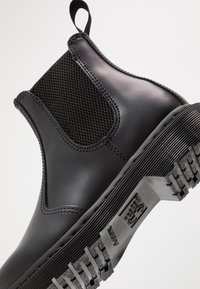 Black ankle chelsea boots featuring a smooth, glossy rubber upper, elastic side panels, and a textured rubber sole with ridges.
