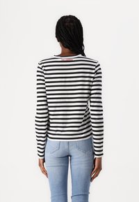 Sorte og hvite stripete langermede skjorter med rund hals, med en rød Karl Lagerfeld-logo på baksiden. Kombinert med lyseblå jeans.
