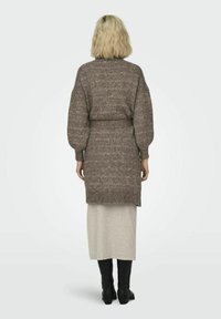 Cárdigan marrón de punto con mangas oversized, cintura ceñida con cinturón y acabado texturizado, combinado con una falda larga gris claro y botas negras hasta la rodilla.