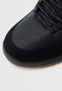 Crna tenisica s glatkim kožnim prednjim dijelom, perforiranim detaljima, semiš naglascima i teksturiranim crnim vezicama, s gumenim potplatom.