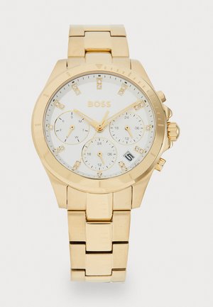 Montre-bracelet dorée avec un cadran rond blanc, index sertis de pierres, trois sous-cadrans et un bracelet en métal à maillons. Présente un affichage de la date.