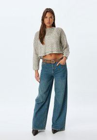 Maglione corto in cotoncina grigio chiaro a maglia, con maniche lunghe; abbinato a jeans in denim blu a vita alta e gamba larga, con una cintura marrone.