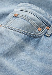 Jasnoniebieska tkanina dżinsowa zbliżenie na przednią kieszeń z miedzianymi nitami i kontrastowymi przeszyciami.