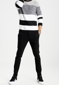 Czarny i biały sweter w paski z dzianiny z szarymi akcentami, z długimi rękawami i prążkowanym dekoltem, w zestawieniu z czarnymi spodniami slim fit i czarnymi sneakersami.