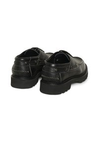Paire de chaussures décontractées en cuir noir avec semelles épaisses rainurées et coutures blanches visibles, vues de dos sur fond blanc.