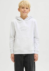 Sudadera gris claro de tejido suave, con un bolsillo canguro y texto bordado "Originals". Las mangas están ajustadas; corte relajado, combinada con pantalones oscuros.