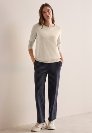 Haut à manches longues gris clair avec un col arrondi associé à un pantalon à rayures bleues marines et des baskets blanches. Tenue décontractée en matériaux doux.