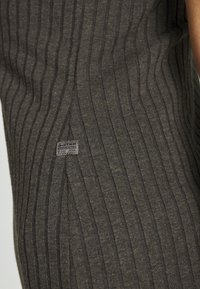 Mörkbrun ribbad tyg med vertikala ränder; har en liten G-Star Originals etikett i det nedre hörnet. Slät textur, skräddarsydd design.