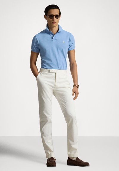 Ανοιχτό μπλε πόλο μπλούζα με μικρό λογότυπο, άσπρο παντελόνι και καφέ μοκασίνια. Γυαλιά ηλίου που συμπληρώνουν το ντύσιμο, απαλό υλικό, κομψή εφαρμογή.