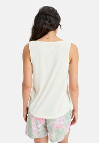 Helles Cremefarbenes Tanktop mit weitem Ausschnitt, kombiniert mit pastellgrünen Shorts mit pinkem Blumenmuster. Weicher Stoff, lässige Passform, keine sichtbaren Beschläge.