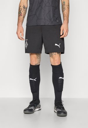 Sorte atletiske shorts med hvid Puma-logo, parret med sorte knæhøje sokker. Teksturert sort skjorte med geometriske mønstre og holdemblem.