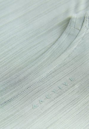 Gaiši zaļa sporta krekla augšdaļa ar gludu, teksturētu virsmu. Ir apaļa kakla izgriezums un drukāta "ACTIVE" logo.