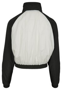 Kappad jacka med svart fram och vit baksida. Har hög krage och elastisk nederkant och ärmar, tillverkad av lättviktsmaterial.