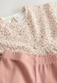 Top floral en crema con patrones marrones y rosas, combinado con pantalones acanalados en rosa suave. Tejido de algodón, ajuste relajado, con cintura elástica.