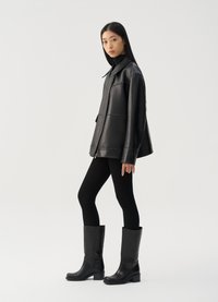 Fekete bőrdzseki, gallérral, bordázott fekete leggings-szel és térd fölé érő fekete csizmával párosítva. Simább textúrájú és minimalista dizájn.