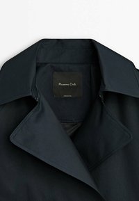 Granatowy płaszcz trench z szerokim kołnierzem, gładką teksturą i czarną metką z napisem "Massimo Dutti". Lekki materiał o prostym wzorze.