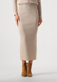Fustă tricotată în bej, cu o textură canelată, design ajustat și lungime până la jumătatea gambei. Asortată cu bocanci din suede maro.