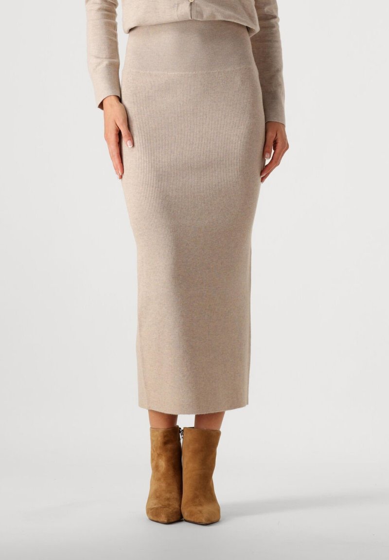 Gebreide rok in beige, met een geribbelde structuur, aansluitend ontwerp en een lengte tot halverwege het kuit. Gepaard met bruin suède enkellaarsjes.
