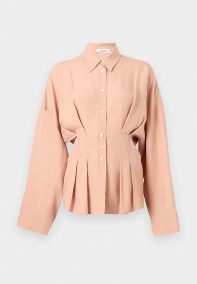 Μακρυμάνικη μπλούζα σε ανοιχτό ροδακινί χρώμα με κουμπιά, μυτερό γιακά και πιετάκια που συγκεντρώνονται στη μέση για εφαρμοστή σιλουέτα.