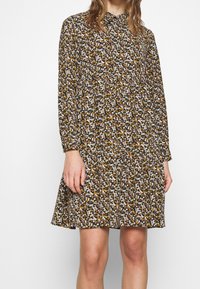 Floral dress features a black background with small white, yellow, and orange flowers. Long sleeves, a gathered waist, and a flared skirt.