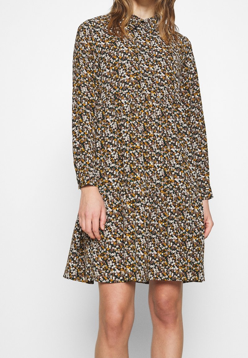 Floral dress features a black background with small white, yellow, and orange flowers. Long sleeves, a gathered waist, and a flared skirt.