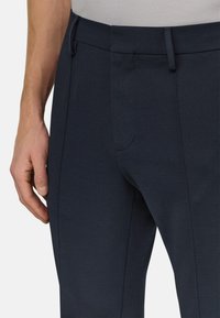 Dunkelblaue Hose mit schlanker Passform, glatter Textur und sauberem Design. Mit vorderen Taschen und einem flachen Bund für eine maßgeschneiderte Optik.