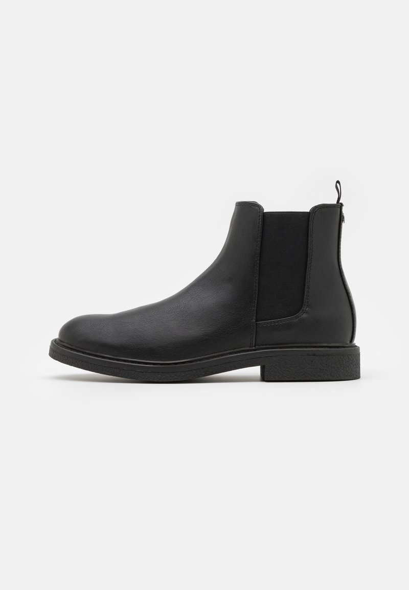 Bottine Chelsea en cuir noir avec panneaux latéraux élastiques, languette de tirage à l'arrière et petit talon bloc, vue de profil sur fond blanc.