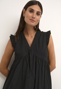 Black dress with a V-neck, ruffled short sleeves, and gathered bodice. Made of a smooth fabric, it features a flowing design.